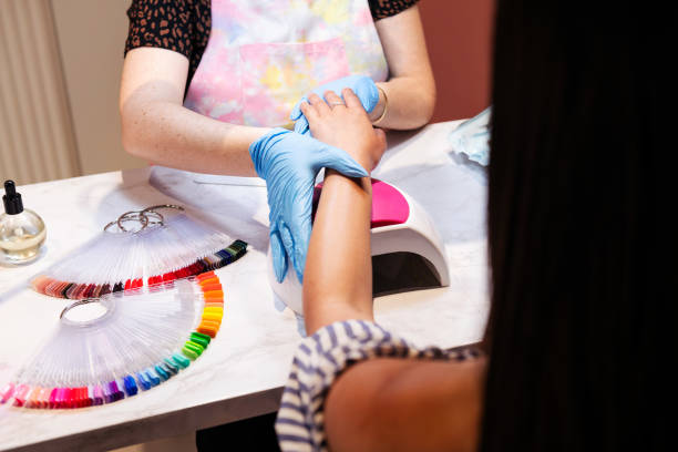 Manicurist applying nail polish to client in salon with color palette visible