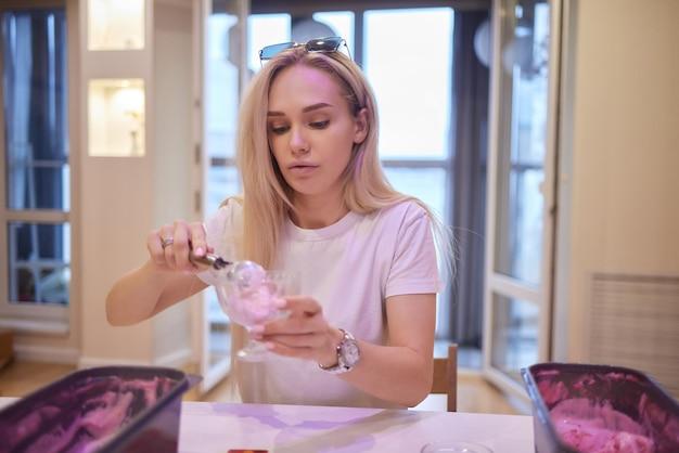 Woman scooping pink ice cream at a table indoors