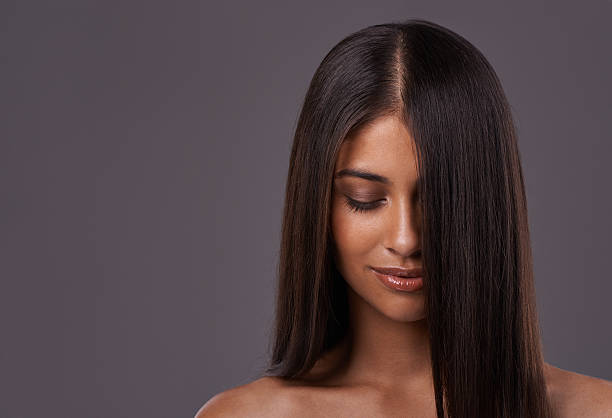 Portrait of a young woman with long straight hair looking down against a gray background