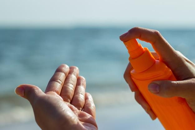 Person applying sunscreen from orange bottle on the beach