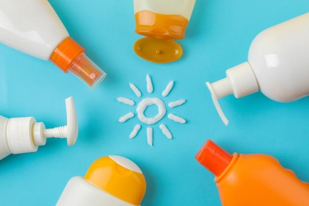 Variety of sunscreen bottles on blue background with a sun symbol made from cream